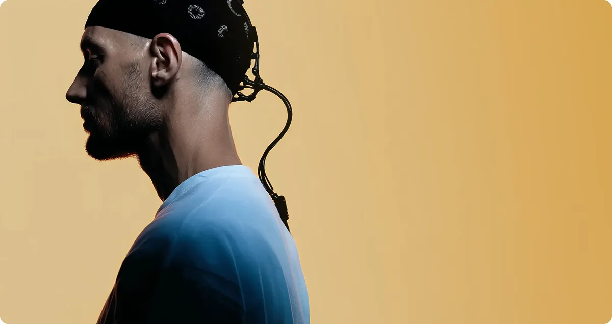 Side profile of a man wearing a black EEG headset against a gradient beige background.