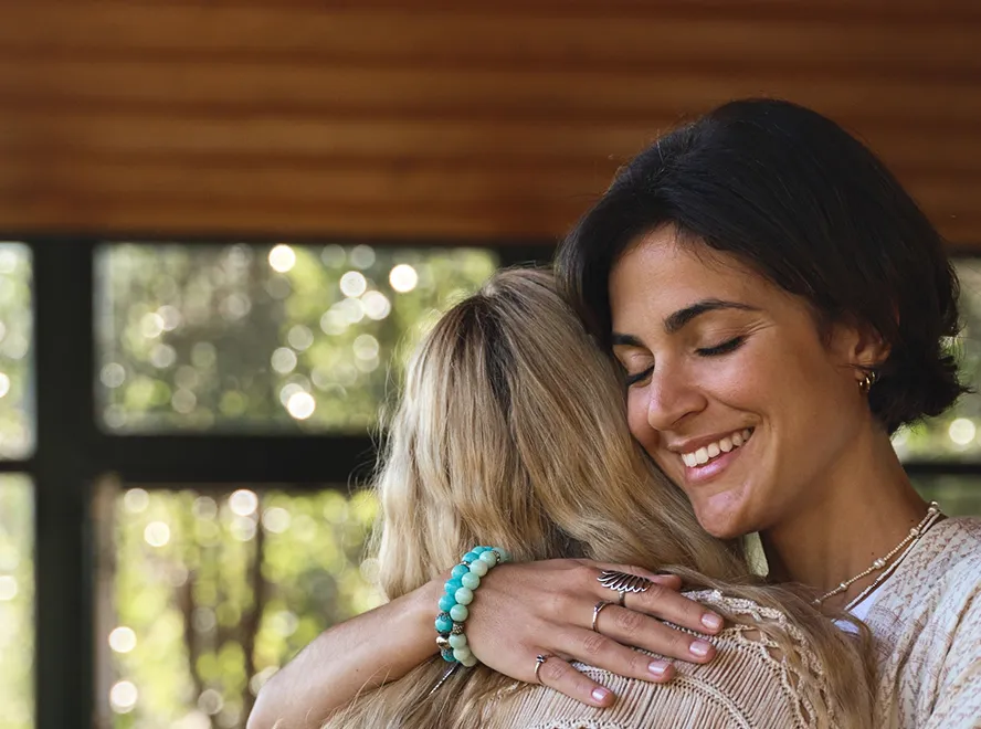 Two women embracing, one smiling with eyes closed while hugging the other from behind.