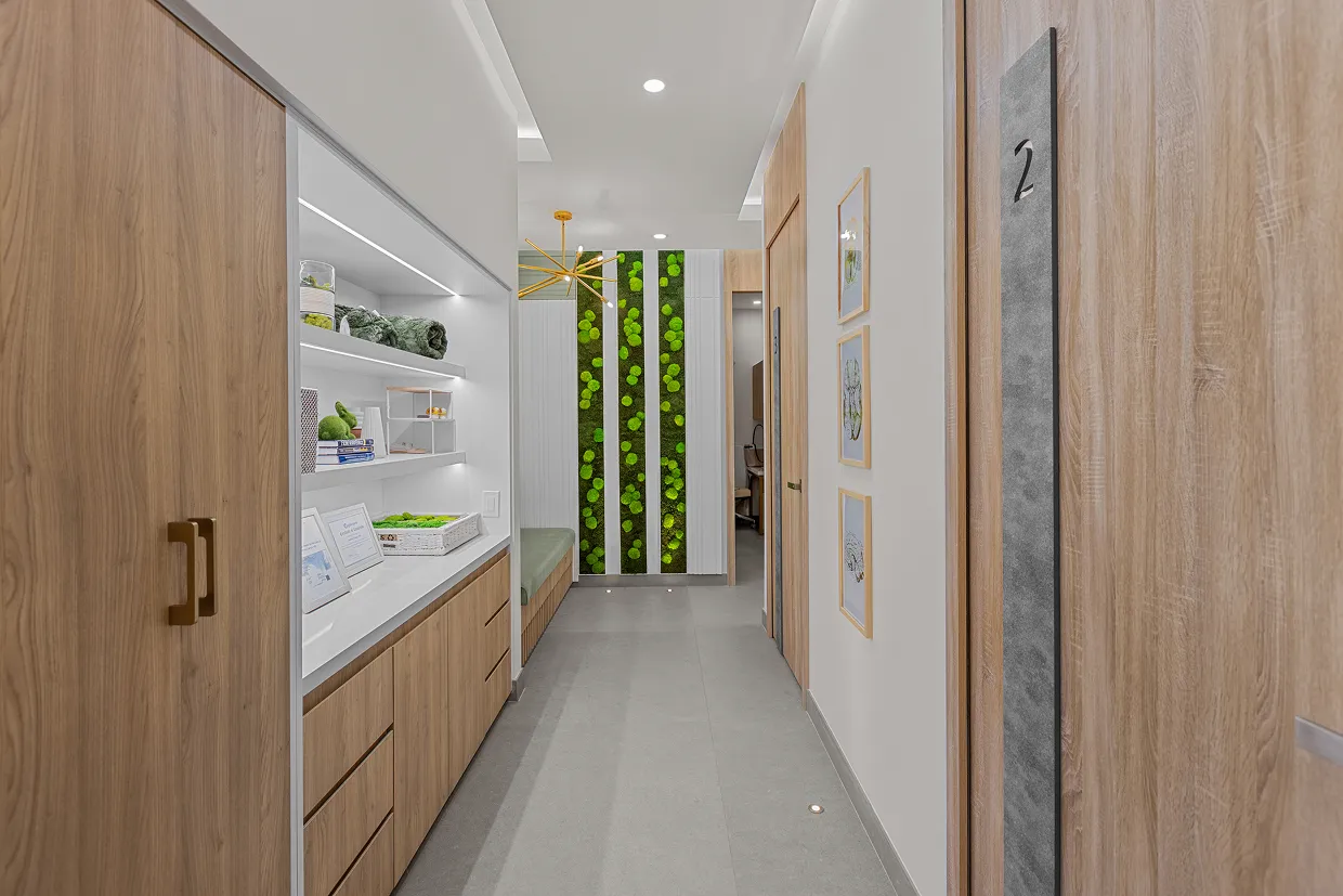 Modern hallway with wood-paneled doors, built-in shelves with decor, green vertical moss wall feature, and gray tile floor.